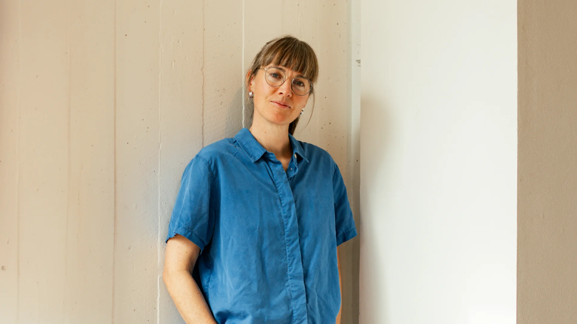 Mette Øyås Madsen i blå skjorte foran væg med lys farve