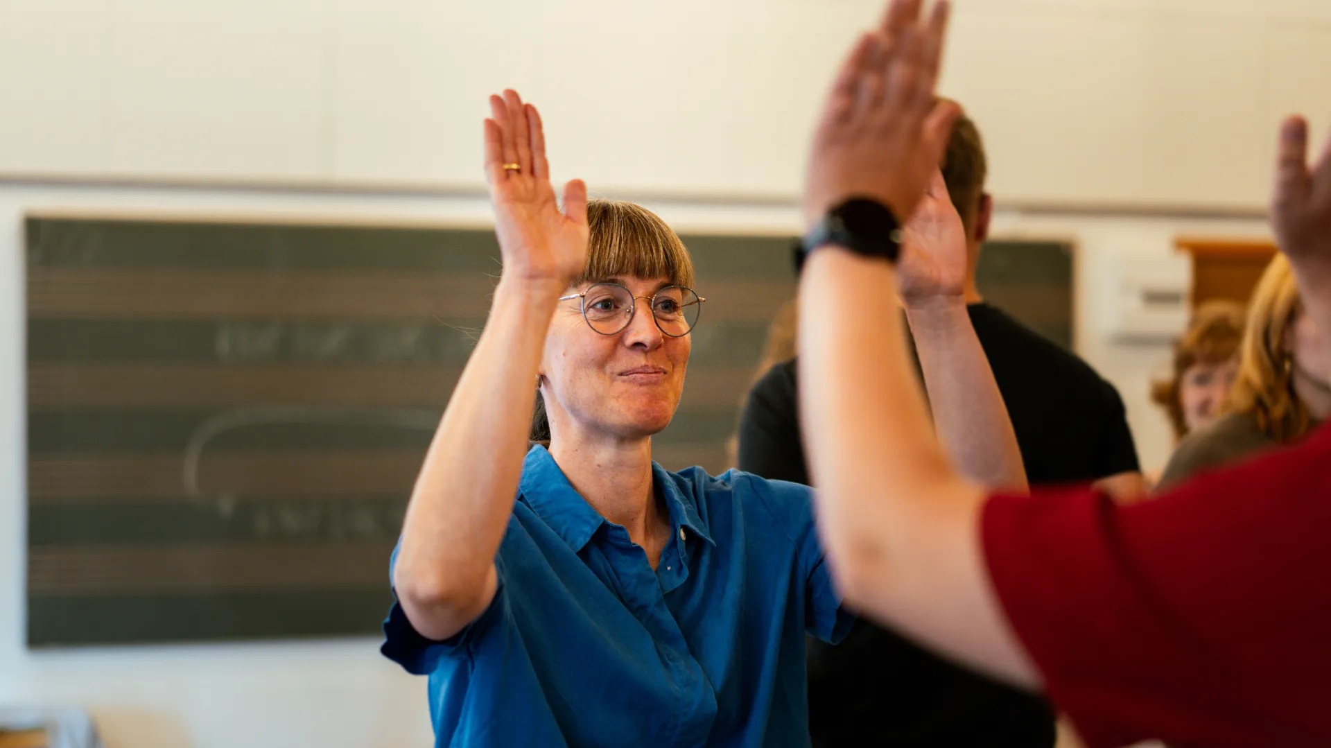 Mette Øyås Madsen med hænderne oppe giver high five til en person, der står med ryggen til.